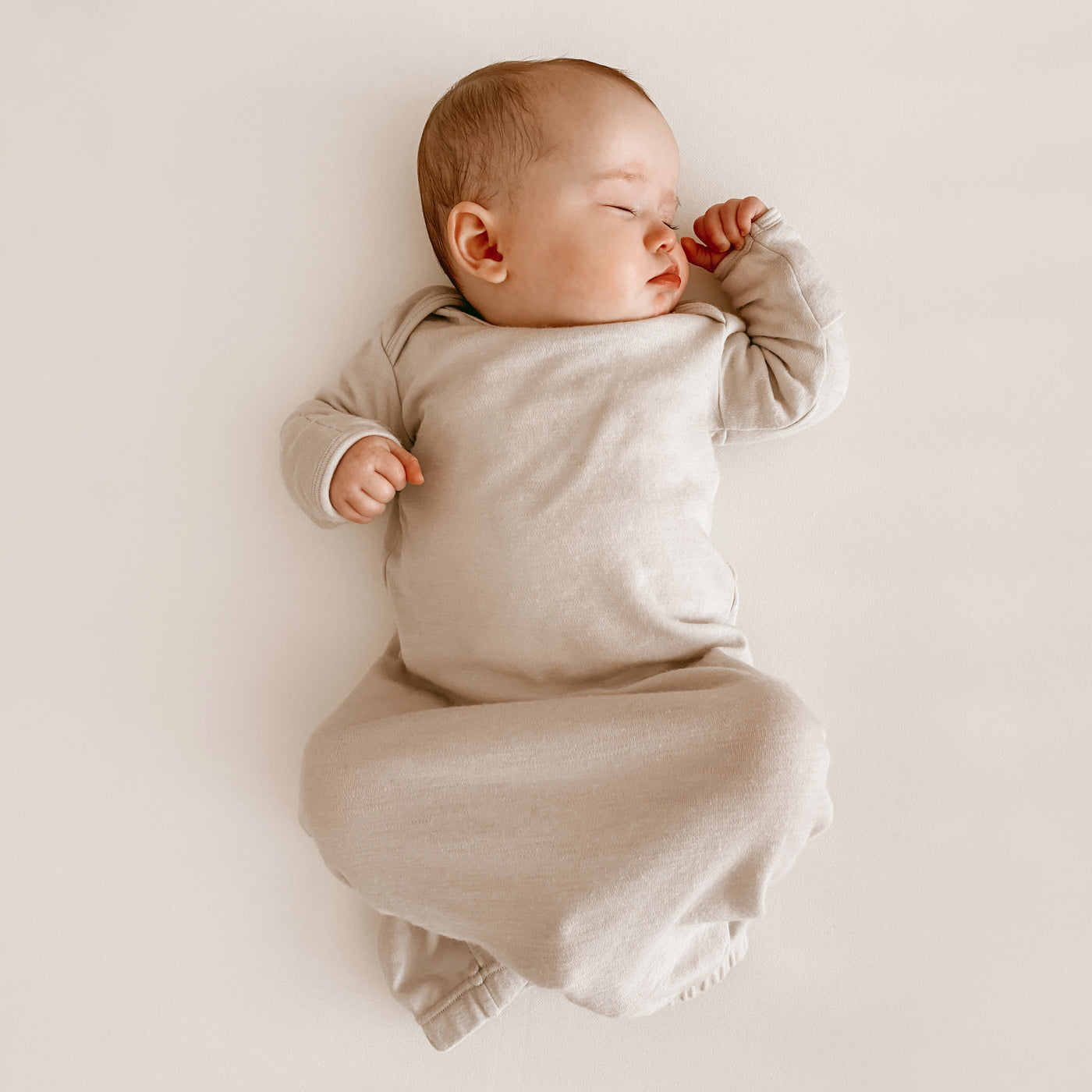 Baby in a beige baby gown lying on a plain cribsheet