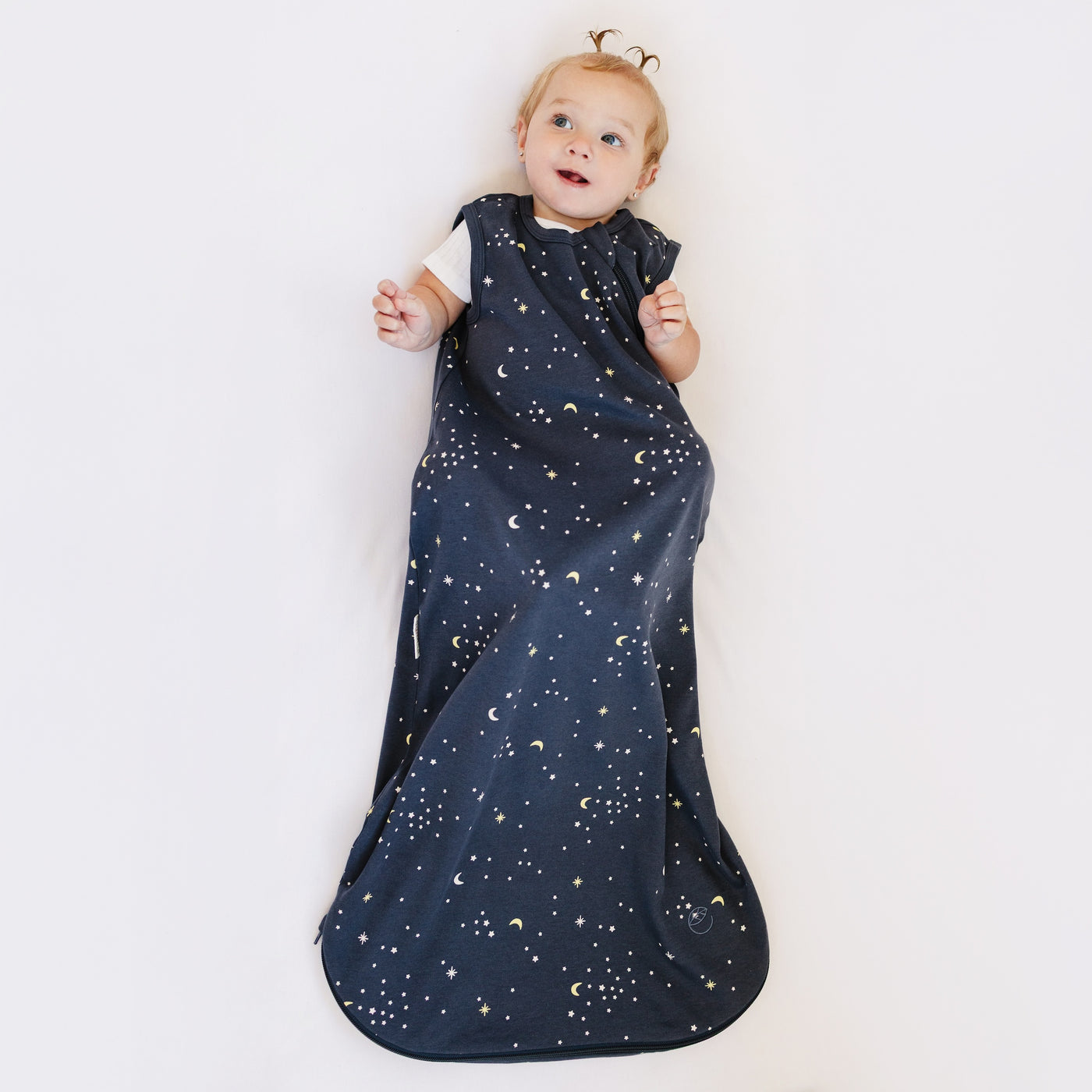 Child wearing a dark blue sleep bag with celestial pattern on a white background