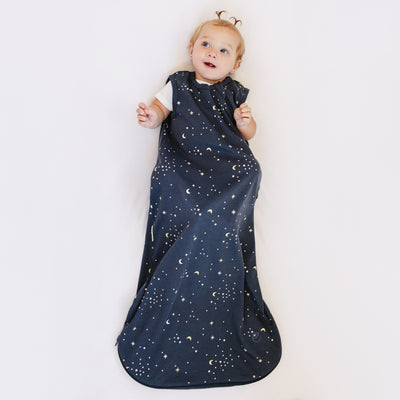Child wearing a dark blue sleep bag with celestial pattern on a white background