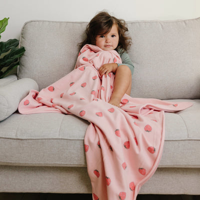 Child wrapped in a pink blanket with strawberry pattern on a gray couch