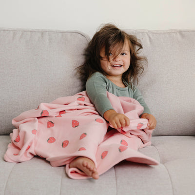 Child sitting on a couch with a pink blanket featuring strawberry patterns