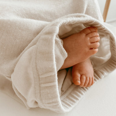 Baby feet peeking out from under a soft beige Woolino baby gown