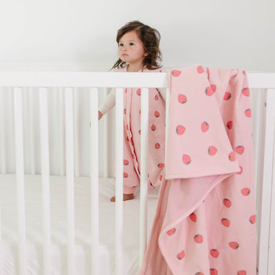Child in a crib with a pink blanket featuring red hearts