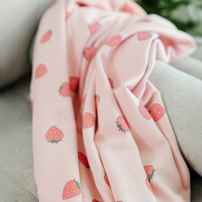 Woolino merino and organic cotton toddler blanket with strawberry pattern draped over a surface