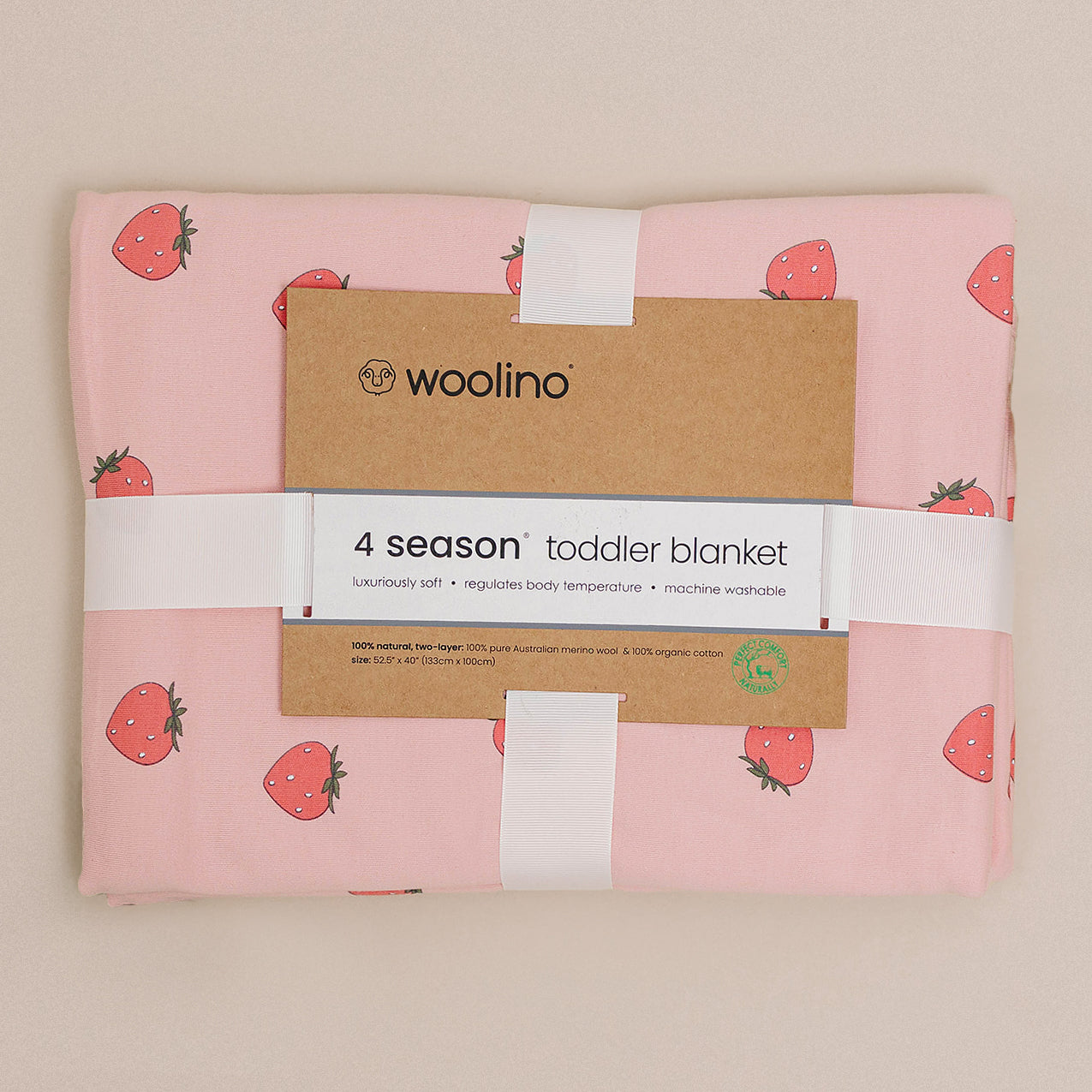 Pink toddler blanket with strawberry pattern and Woolino branding on a beige background