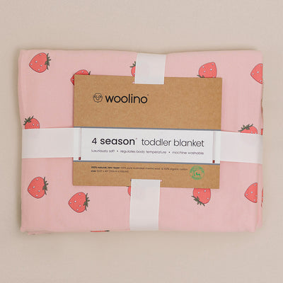 Pink toddler blanket with strawberry pattern and Woolino branding on a beige background