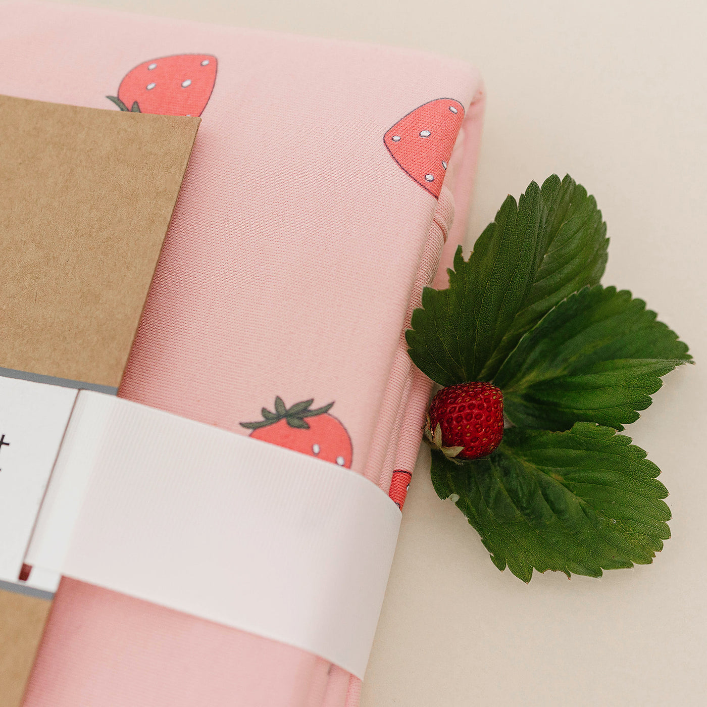 Pink fabric with strawberry pattern and a real strawberry on a white background